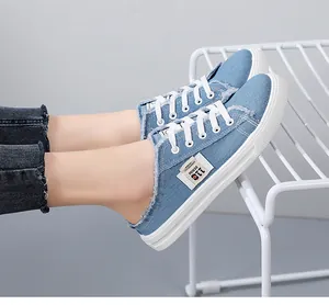 Close-up detail of blue denim slip-on sneakers featuring white laces and distressed raw edges