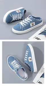 Top view of casual blue denim mule sneakers with frayed edges, white laces, and rubber sole.