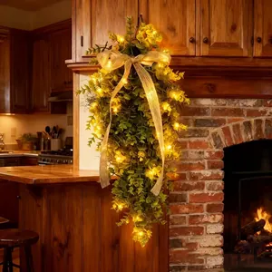 Warmly lit artificial eucalyptus teardrop wreath with a burlap bow on wooden cabinet