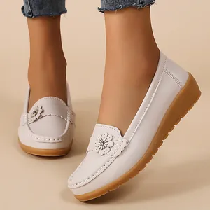Close-up of white loafers with flower detail and textured brown rubber sole.