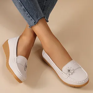 Detail of white wedge loafers with flower ornament worn by a model.
