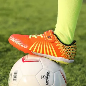 Vibrant orange children's turf soccer shoes for professional training on grass field.