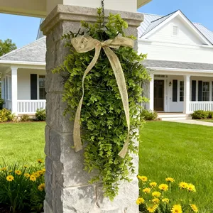 Detailed view of faux greenery teardrop wreath with burlap bow hanging on a rustic stone pillar