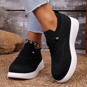 Detailopname van zwarte ademende fly-knit sneakers met dikke witte zolen aan voeten
