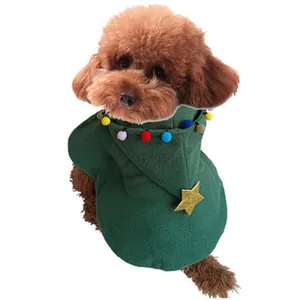 Close-up of a brown poodle wearing a festive green Christmas pet cape with colorful pom-poms.