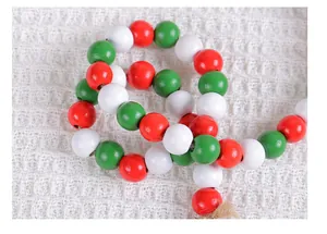 Close-up of red, white, and green wooden Christmas beads on a white textured fabric background