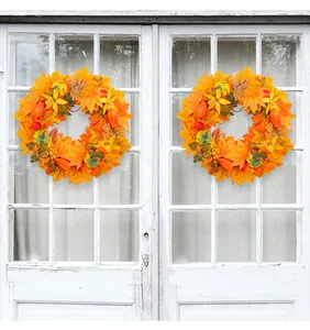 Detailed view of two autumn wreaths with maple leaves and pumpkins on a white door