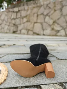Primo piano di stivale alto in camoscio nero con tacco largo marrone e zip laterale.