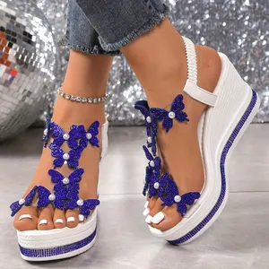 Nahaufnahme von weißen Keilsandaletten mit glitzernden blauen Schmetterlingen.