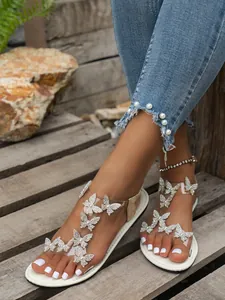 Primer plano de sandalias planas elegantes con pedrería de mariposa y tiras claras.