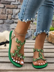 Detalle de sandalias planas con mariposas de strass verdes y correas de PVC para la playa