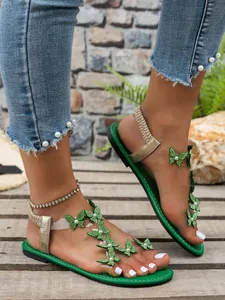 Primer plano de sandalias planas verdes con brillantes decoraciones de mariposas de strass.