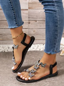 Detalle de sandalias negras planas con adornos de mariposas de diamantes de imitación