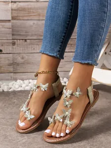 Detalle de adornos de mariposa con diamantes de imitación en sandalias planas.