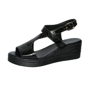 Détail d'une sandale compensée noire avec texture croco et boucle.