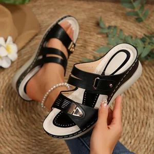 Detailed macro view of black wedge sandals with gold buckle and laser-cut patterns.