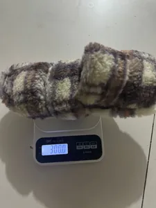 Detalle de una zapatilla de felpa a cuadros pesada en una báscula de cocina, peso 300g.