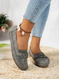 Détail de mocassins en maille grise avec pompons et motifs découpés