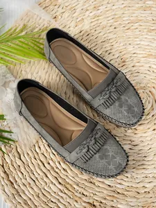 Vue détaillée de mocassins gris avec franges et motifs perforés sur tapis de paille