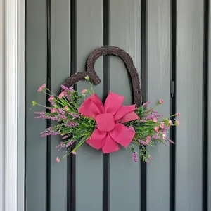 Herzförmiger Kranz mit rosa Schleife und Kunstblumen an einer dunklen Tür