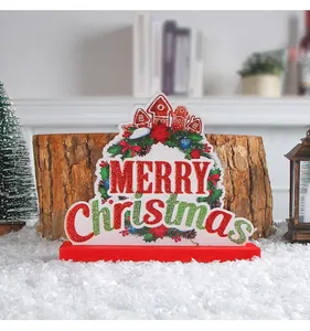 Detail of 'MERRY Christmas' wooden sign with gingerbread house and wreath design.