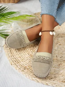 Détail de mocassins plats beiges pour femmes avec franges et motifs ajourés sur un modèle.