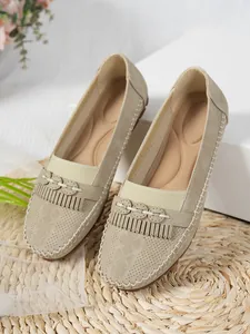 Gros plan de mocassins beiges pour femmes avec pompons et texture en daim perforé