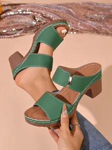 Gros plan de mules vertes à talons épais avec surpiqûres blanches et boucle dorée.