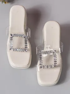 Detail of women's chunky heel slides featuring a clear strap and square rhinestone buckle