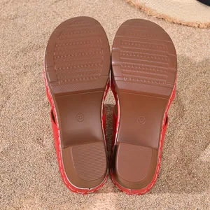 Vue détaillée des semelles brunes de sandales rouges à talons hauts sur sable de plage