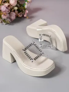 Close-up detail of cream platform high-heel slippers with rhinestone buckle and clear strap