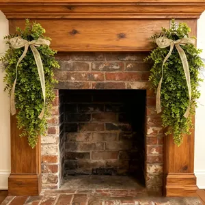 Pair of lush artificial greenery swags with burlap bows on a rustic fireplace