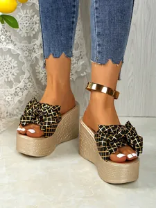 Detailed view of women's summer wedge sandals featuring a large gold grid bow and platform