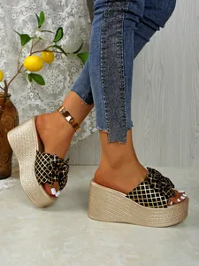 Close-up detail of golden woven platform wedge sandals with black and gold bow