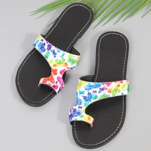 Detail van zomerse platte sandalen met een kleurrijke vlinderprint en teenlus
