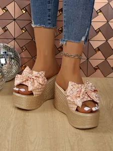 Close-up detail of stylish pink bow wedge sandals with gold grid pattern on platform sole.