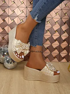 Close-up of elegant platform wedge sandals with gold checkered bow and woven texture