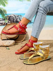 Detail von flachen Zehensandalen in Rot und Gold mit Doppelbuckle am Strand.