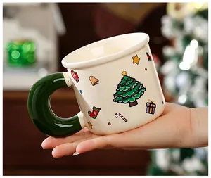 Gros plan d'une main tenant un mug de Noël rétro festif avec une grande anse verte.