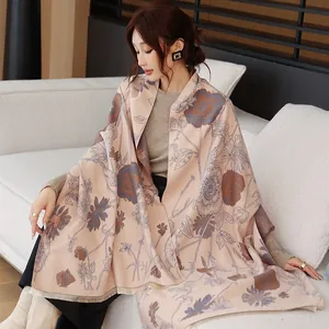 Close-up of large beige pashmina shawl with blue ink-wash floral print draped over a woman.