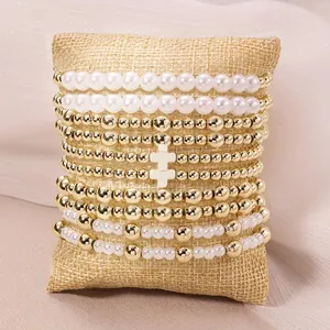 Gros plan d'un ensemble de 5 bracelets superposés avec perles, billes dorées et une croix.