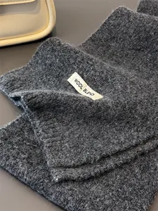Detailansicht eines grauen Strickschals aus Wollmischung mit eingewebtem Materialetikett
