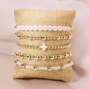 Détail d'un ensemble de 5 bracelets avec perles dorées, perles et breloque croix blanche.