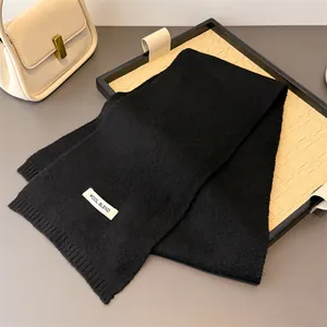 Nahaufnahme eines weichen, schwarz gestrickten Wollmischschals mit schlichtem Etikett.