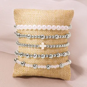 Détail de 5 bracelets élastiques empilables avec perles et croix sur jute.