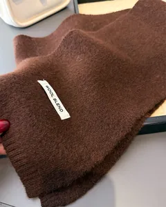 Makro-Detailansicht eines braunen Strickschals aus Wollmischung mit Textur und Materialetikett.