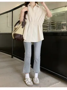 Full body shot of a woman in a cream waist-cinching short sleeve shirt and blue jeans