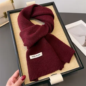 Detail eines weinroten Strickschals mit Wool Blend Etikett auf einem geflochtenen Tablett
