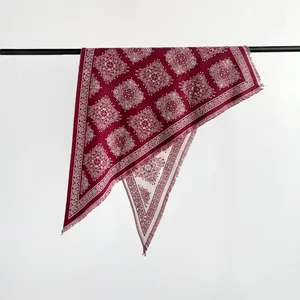 Detailed view of burgundy triangle scarf with white paisley pattern and fringed edges