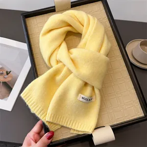 Detailaufnahme eines weichen gelben Strickschals mit Wollmischungs-Etikett